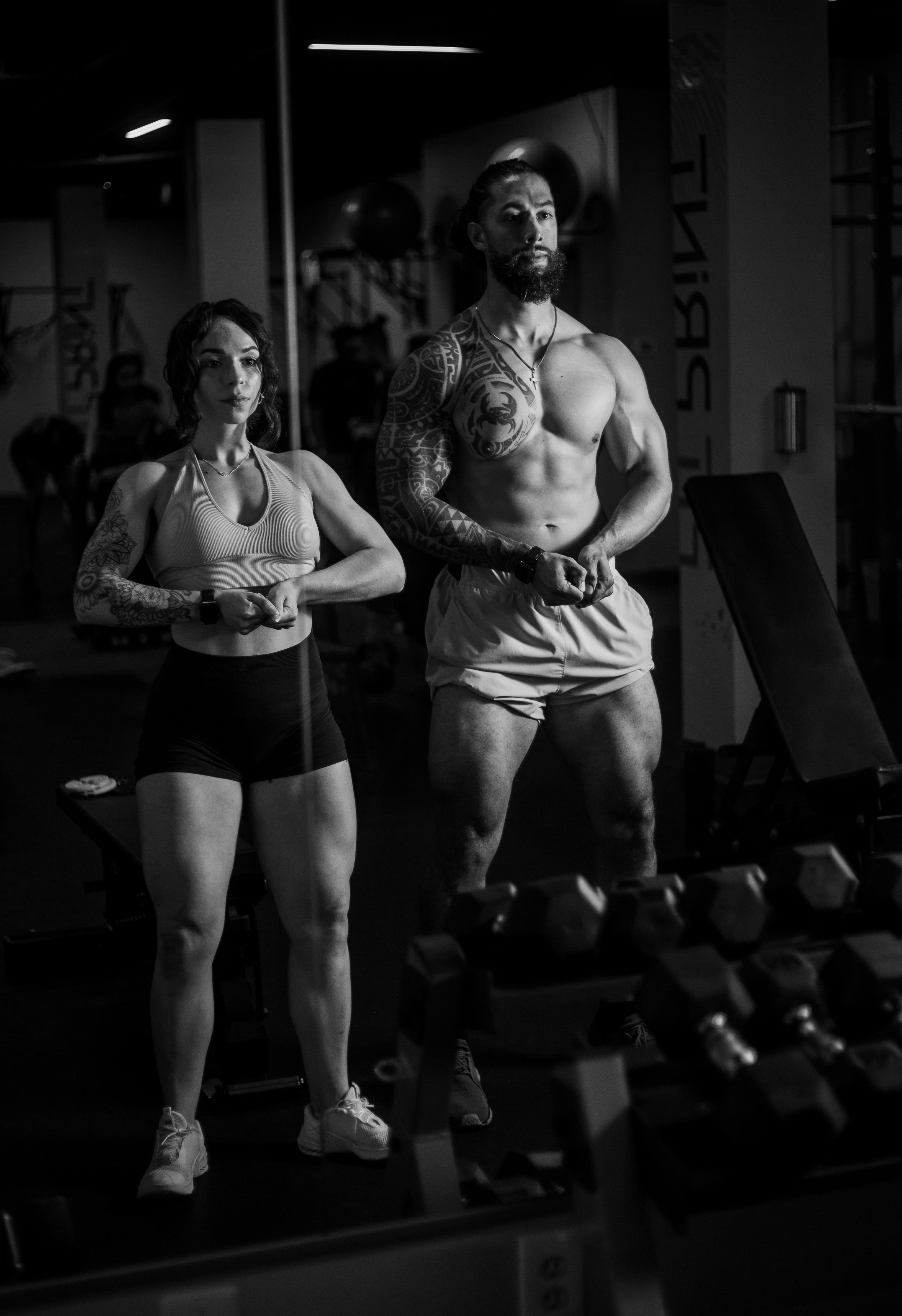 Two fit bodybuilders posing in a monochrome gym setting, showcasing strength and focus.